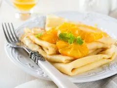 Deliziose crepes senza uova, guarnite con spicchi d'arancia succosa e foglioline di menta fresca. Un piatto leggero e gustoso.