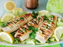 Tre calamari alla griglia, conditi con aglio e prezzemolo, serviti su un letto di lattuga con spicchi di limone.