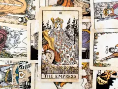 Karta Tarota "The Empress" w otoczeniu innych kart. Królowa siedzi na tronie, trzymając berło, symbolizując płodność i obfitość.