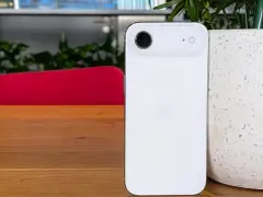 Biały iPhone z 4 aparatami, leżący na drewnianym blacie obok doniczki.