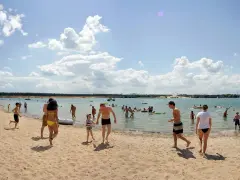 Menschen genießen einen sonnigen Tag am Badesee Frankfurt. Kinder planschen im Wasser, während Erwachsene sich am Sandstrand entspannen.