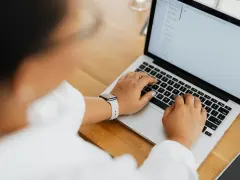 Kobieta pisze na laptopie, na ekranie widać artykuł po niemiecku.