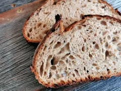 Zwei Scheiben rustikales Sauerteigbrot mit großer Porung liegen auf einem Holzbrett. Die Sauerteig Vorteile sind offensichtlich: ein toller Geschmack und eine bekömmliche Textur.