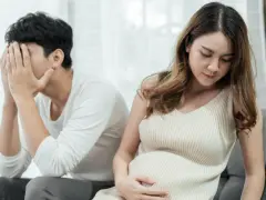 Ein Mann mit verdecktem Gesicht sitzt abgewandt von einer schwangeren Frau. Die Szene deutet auf eine Trennung in der Schwangerschaft hin, die mit Kummer verbunden ist.