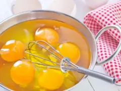 Pięć żółtek w metalowej misce z trzepaczką. Idealne, by dowiedzieć się, co zrobić z żółtek na pyszne ciasto.