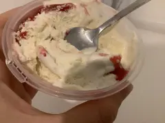 Ein Löffel steckt in einem Becher mit schmelzendem, altem Eis mit Erdbeersauce.