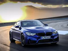 Niebieskie BMW M2 CS pędzi po torze wyścigowym podczas zachodu słońca.