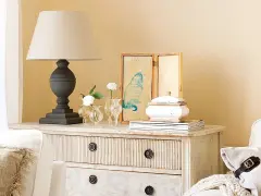 Cómoda de estilo vintage con cajones pintados a la tiza, decorada con lámpara, jarrones con flores y un cuadro de gato.