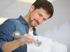 Mężczyzna w dżinsowej koszuli montuje karnisz, przekładając go przez kółka zasłony.