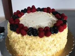Pyszny tort śmietankowo-malinowy z mascarpone, ozdobiony świeżymi malinami i borówkami, posypany złotymi i srebrnymi kuleczkami.
