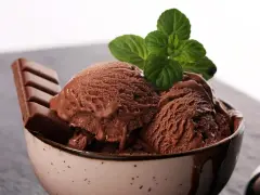 Delicioso helado de chocolate cremoso en un tazón, adornado con una hoja de menta y una barra de chocolate.