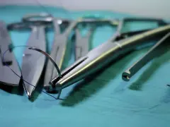 Chirurgiczne narzędzia, w tym igłotrzymacz z nicią, skalpel i pęseta, gotowe do akcji. To kluczowe elementy w specjalizacji operacyjnej.