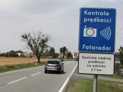 Znak "Kontrola prędkości Fotoradar" informuje, że czy fotoradar musi być oznakowany. Obok droga i pola.