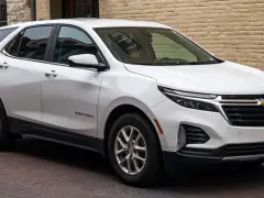 Biały Chevrolet Equinox stoi zaparkowany na brukowanej ulicy, obok ceglanego budynku.
