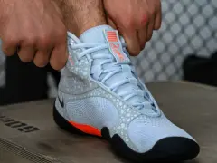 Ręce zapinają jasnoniebieskie buty sportowe z pomarańczowymi akcentami, przypominające styl Batistini.