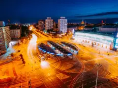 Widok z lotu ptaka na nocne miasto z długimi smugami świateł samochodowych i tramwajowych.