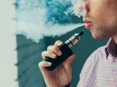 Hombre vapeando, exhala humo blanco. El vapear sube la tensión, cuidado con tu salud.