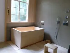 Un baño japonés con tina de madera, ducha y un pequeño taburete. El letrero de madera indica "男湯" (baño de hombres).
