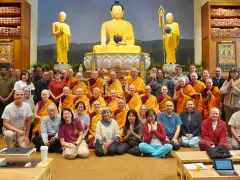 A large group of monks and laypeople gather for a photo in front of a golden Buddha statue, celebrating their shared religion.