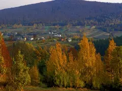 Jesienny krajobraz z kolorowymi drzewami i domami w dolinie. W tle widać łagodne **góry świętokrzyskie szczyty** porośnięte lasem.