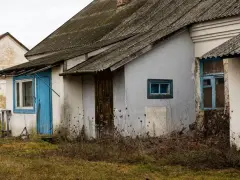 Stary dom z niebieskimi drzwiami i oknami, zarośnięty chwastami. Budowa domu w granicy działki wymaga zgody sąsiada.