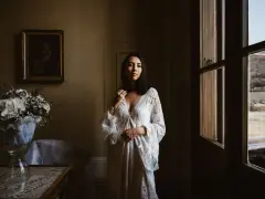 Kobieta w białej sukni, obok bukiet kwiatów. Scena sugeruje przygotowania do ślubu za granicą, co wyjaśnia przyczyny popularności wesel typu "destination wedding".