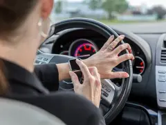 Frau tippt auf ihre Smartwatch am Steuer. Handy am Steuer Strafe vermeiden!