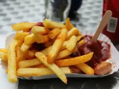 Złociste frytki po wietnamsku, posypane przyprawami, podane z sosem i kiełbaską na papierowym talerzyku.