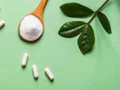 Vita C-vitaminer i kapslar och pulver på en sked, med gröna blad.