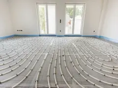 Instalacja ogrzewania podłogowego w bloku. Białe rurki ułożone na siatce tworzą wzór, przygotowane do wylania posadzki.