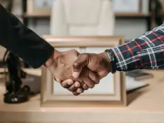 Uścisk dłoni symbolizujący udaną **pracę w Anglii**. Dwie osoby, jedna w czarnej marynarce, druga w kratowanej koszuli, potwierdzają porozumienie.