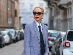 Mujer con traje a cuadros, camisa blanca y corbata negra, luciendo un impecable tomboy style. Gafas de sol y labios rojos completan su look.