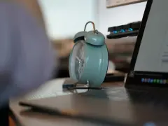 Budzik obok laptopa przypomina o pracy. 3/4 etatu ile to godzin? Czas na efektywność!