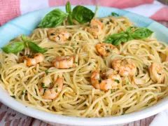 Un plato de espaguetis con gambas, adornado con hojas de albahaca fresca y perejil picado.