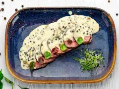 Fette fettine di filetto al pepe verde, ricoperte da una cremosa salsa, guarnite con germogli freschi e foglie verdi.
