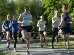 En grupp kvinnor tränar löpning utomhus. De springer i ett parkliknande område, redo att springa 1 km tid.