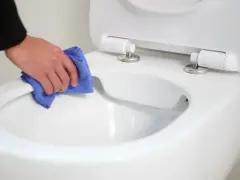 Main propre avec un chiffon bleu, nettoyant le bord d'un wc avec bride ou sans bride.