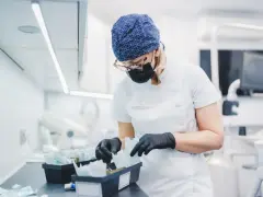 Dentystka w czepku i masce przygotowuje materiały, w tym te do zabiegów z użyciem abrazji powietrznej.