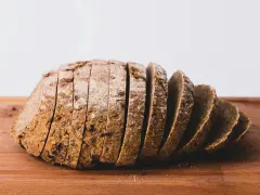 Pokrojony bochenek chleba żytniego na drewnianej desce. Zastanawiasz się, ile kcal ma kromka chleba?