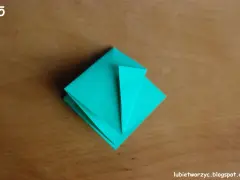 Krok 15 instrukcji, jak zrobić kwadrat z papieru. Turkusowa origami na drewnianym tle.