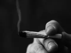 A hand holds a lit joint, smoke curling upwards. This image prompts reflection on whether Christians can smoke weed.