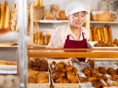 Starsza pani piekarz z uśmiechem układa świeże croissanty. To ulga dla pracujących seniorów, którzy wciąż mają pasję.