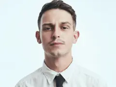 Młody mężczyzna, Vito Bambino, w białej koszuli i czarnym krawacie. Jego wzrost jest imponujący, a spojrzenie intensywne.