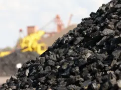 Góra węgla kamiennego, w tle maszyny górnicze. Zastanawiasz się, ile kosztuje tona węgla?