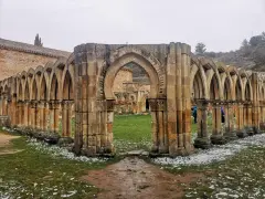 Ruinas de un claustro con arcos de piedra, evocando el nacimiento del Duero. Nieve ligera cubre el césped.