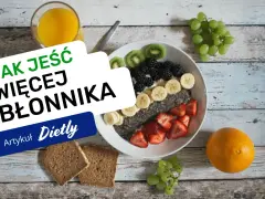 Pyszna owsianka z owocami i nasionami chia, idealna na śniadanie, które ma duzo blonnika. Obok szklanka soku i kromki chleba.