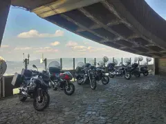 Motocykle pod betonowym zadaszeniem, z widokiem na krajobraz przypominający szwajcarskie Czechy.