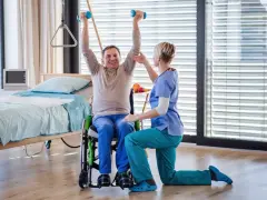 Starszy mężczyzna w wózku ćwiczy z hantlami pod okiem fizjoterapeutki. Czy rehabilitacje można odliczyć od podatku?