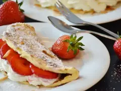 Pyszny omlet z białek z bitą śmietaną i truskawkami, posypany cukrem pudrem i płatkami migdałów.