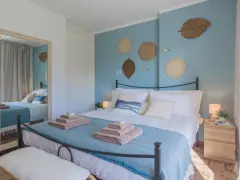 Idee camera da letto: letto matrimoniale con biancheria azzurra e cuscini bianchi, decorazioni a forma di foglia e pesci sulla parete blu.